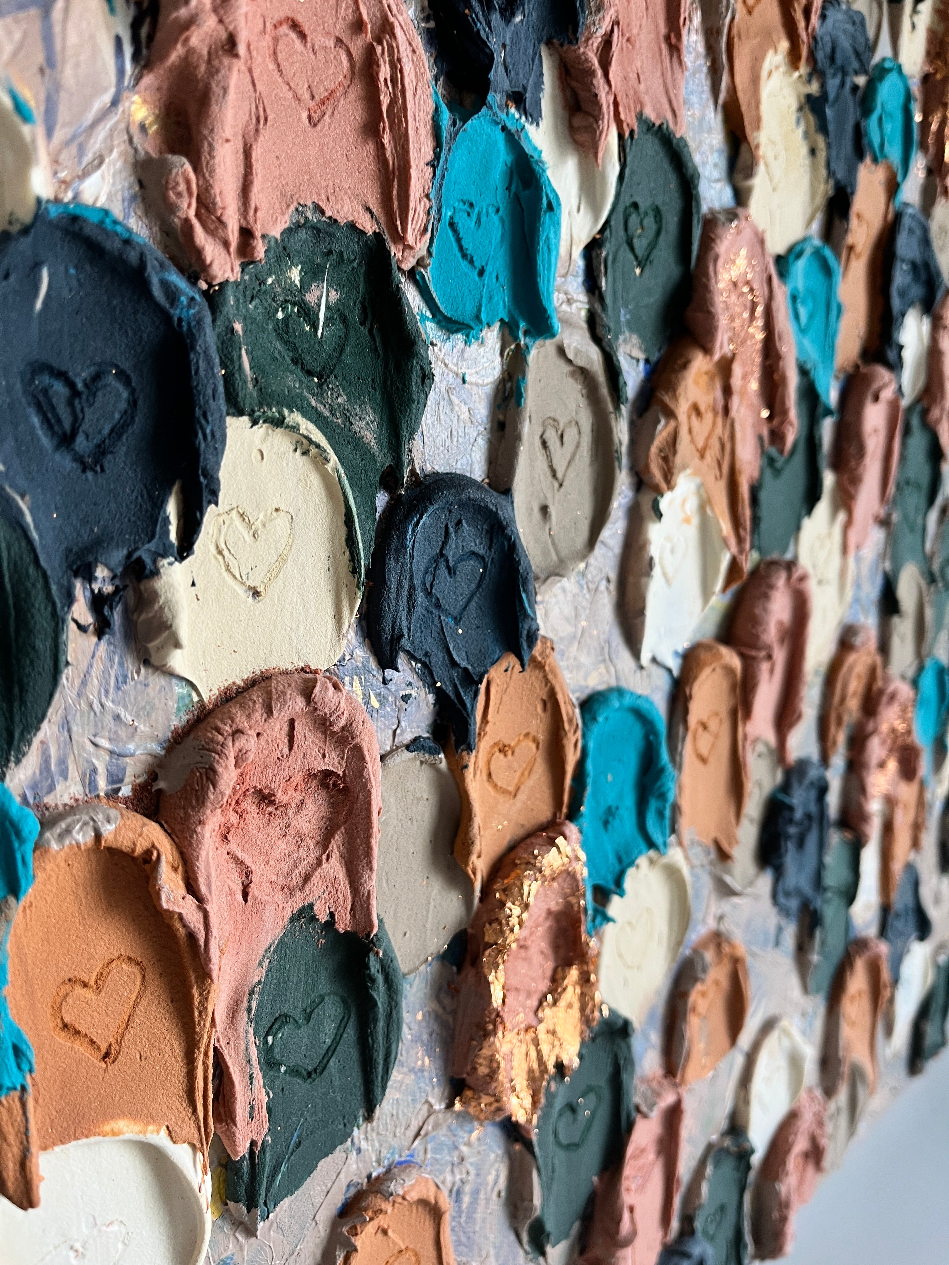 A close-up view of a canvas painting consisting of multiple heart shapes in various colors including blue, brown, beige, and white.