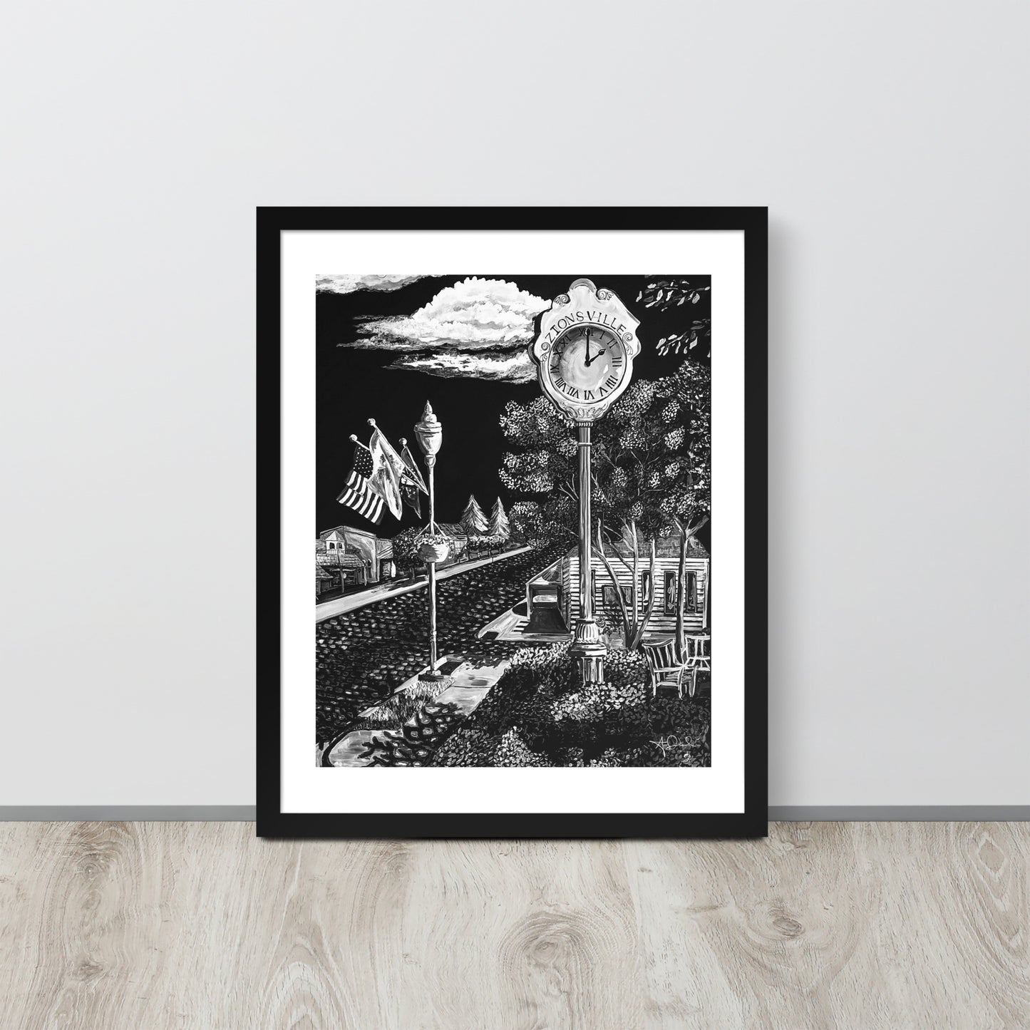 matte black and white framed art print of small town in black frame leaned up against gray wall on light toned wood floor