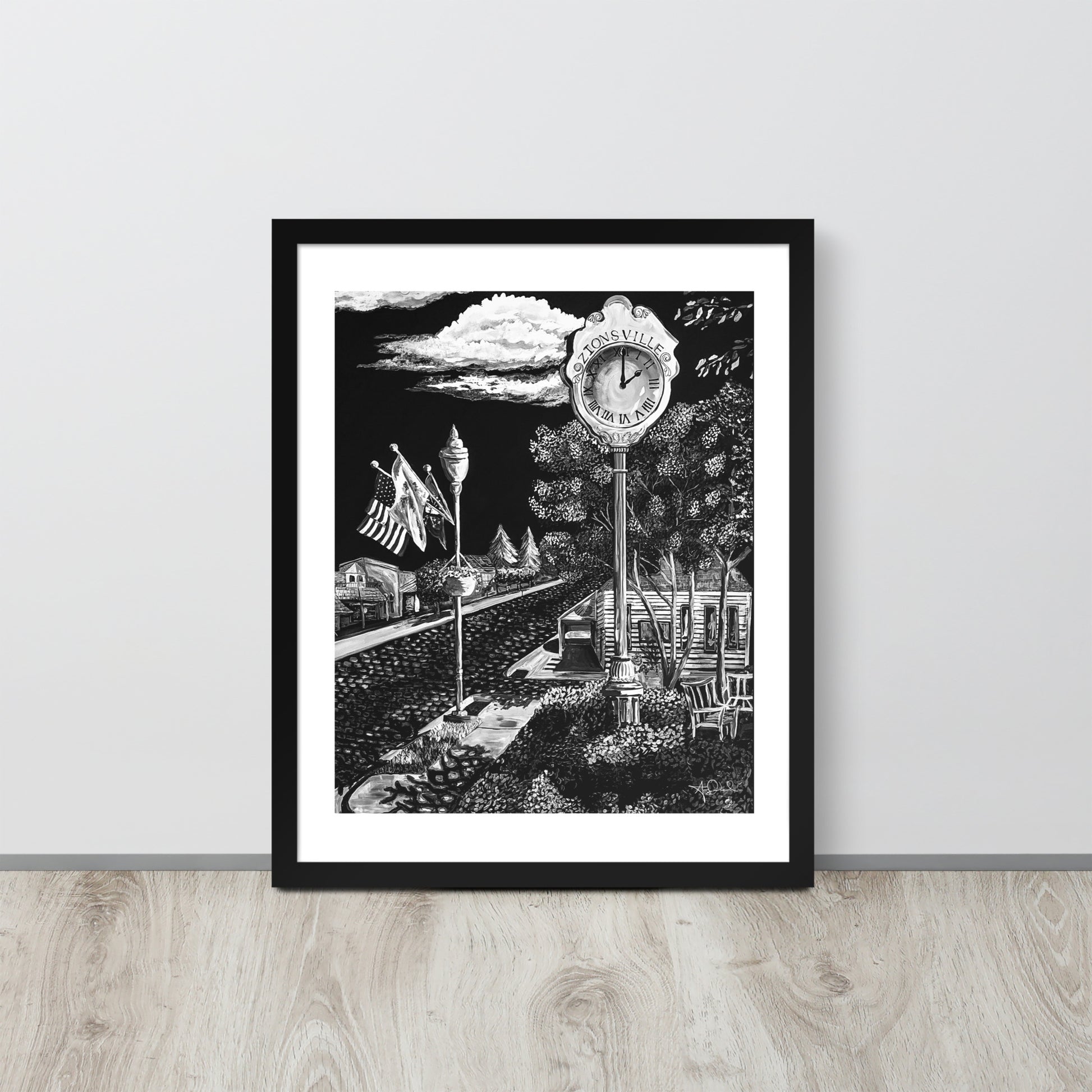 matte black and white framed art print of small town in black frame leaned up against gray wall on light toned wood floor