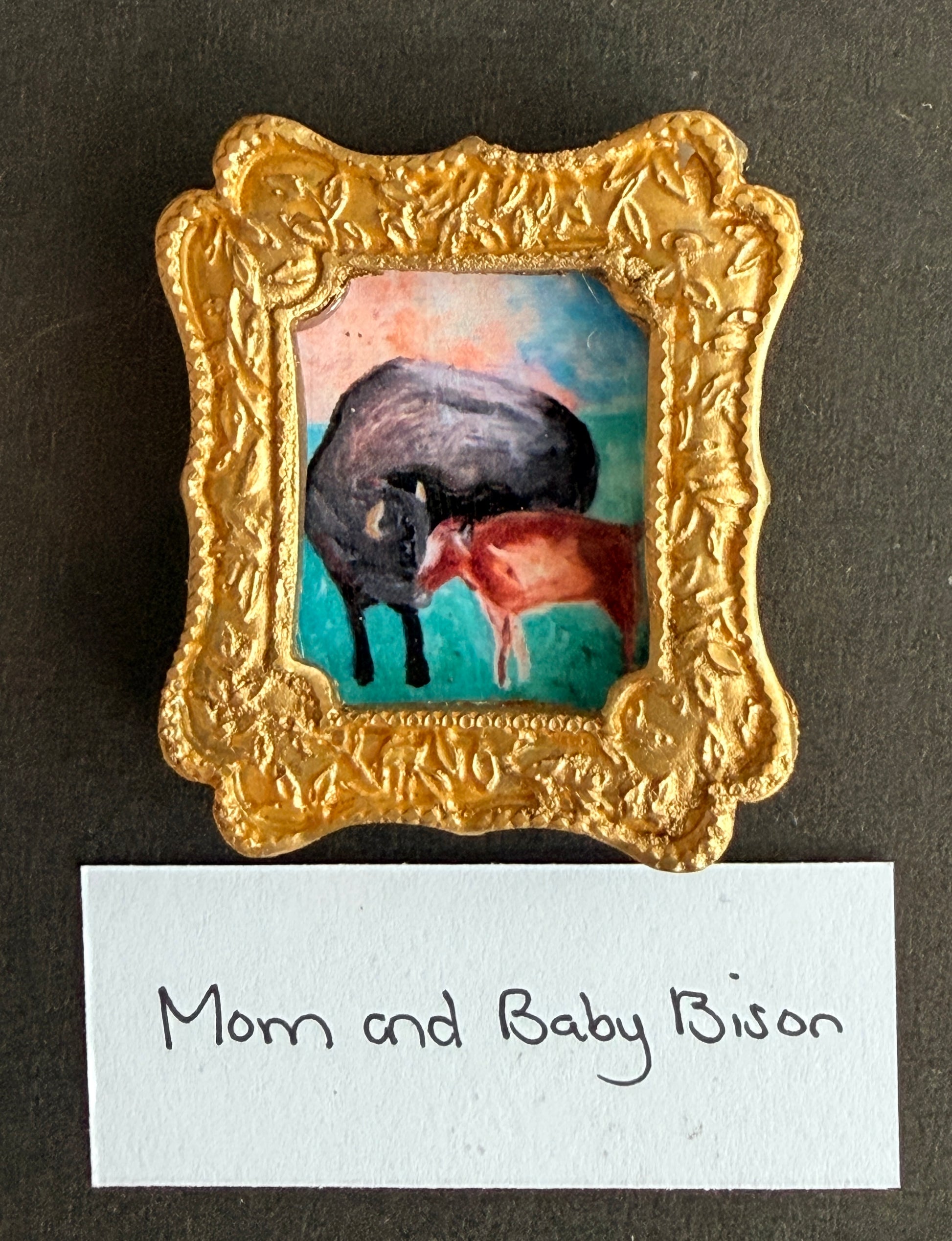 A dreamy colored painting of a mom and her baby bison in a gold frame fridge magnet with the words Mom and Baby Bison below it
