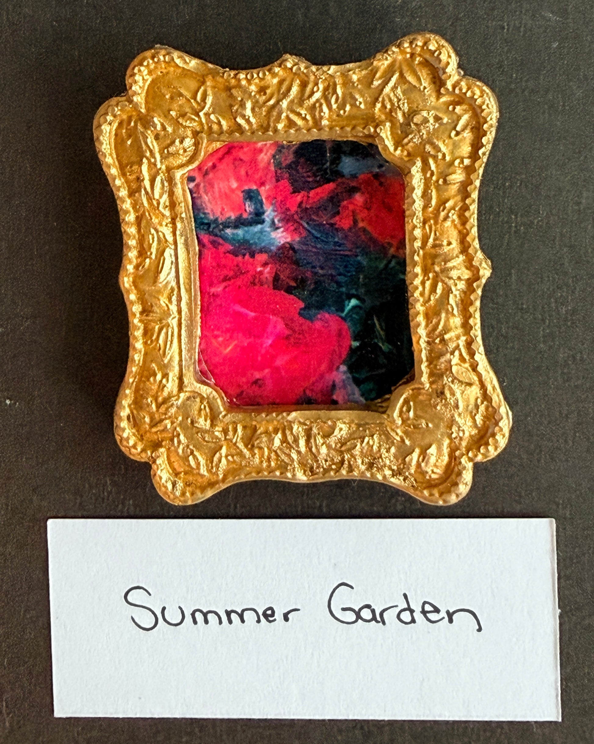 A vibrant red and green abstract painting in a small gold frame fridge magnet with the words Summer Garden below