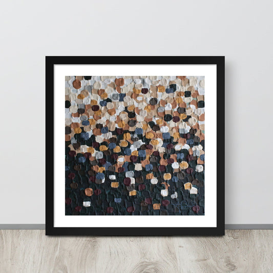 An abstract pointillism piece of framed art in a black frame is leaned up against a white wall