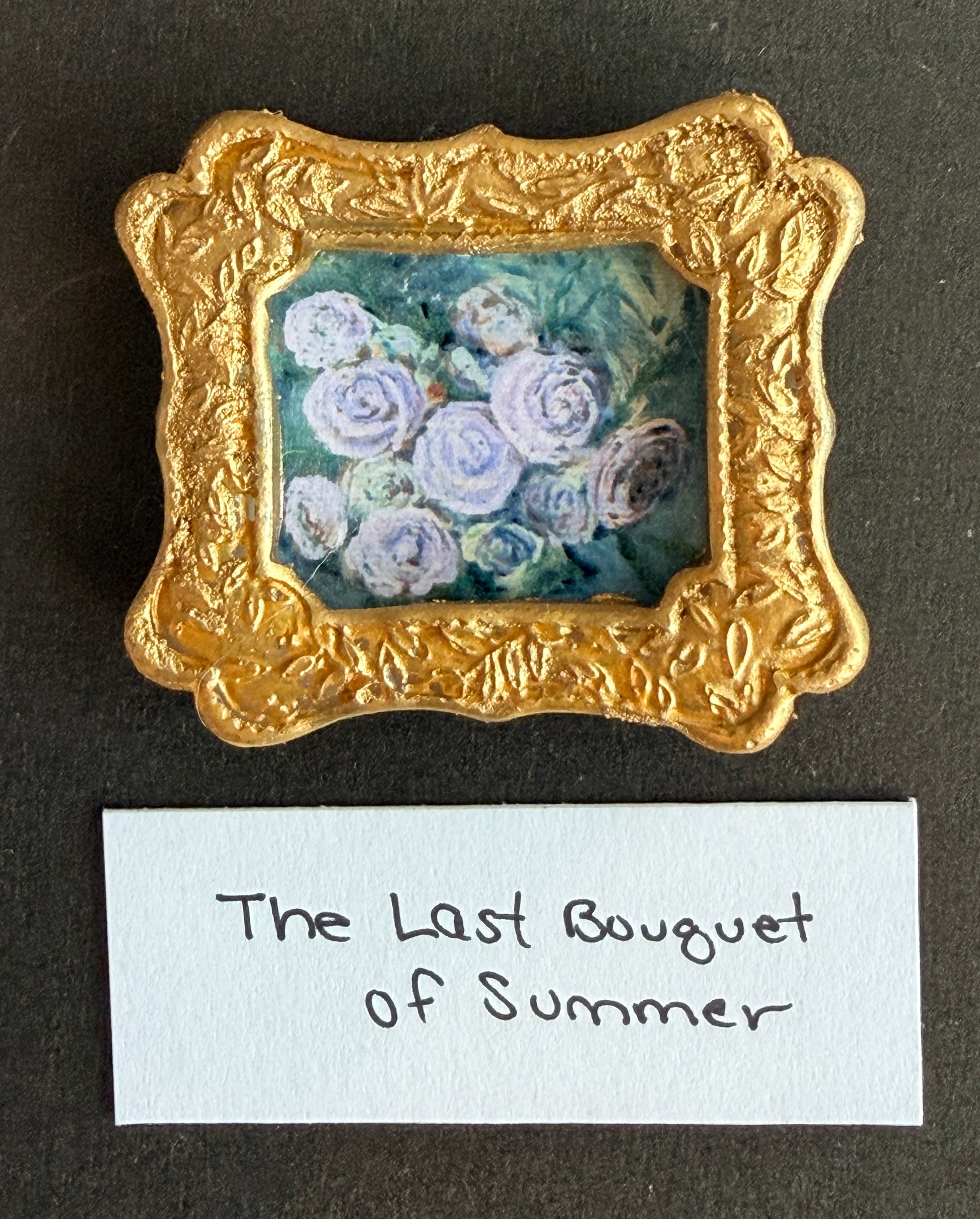 A painting of white roses on a light green blue background in a small gold frame. The words The Last Bouquet of Summer are below. 