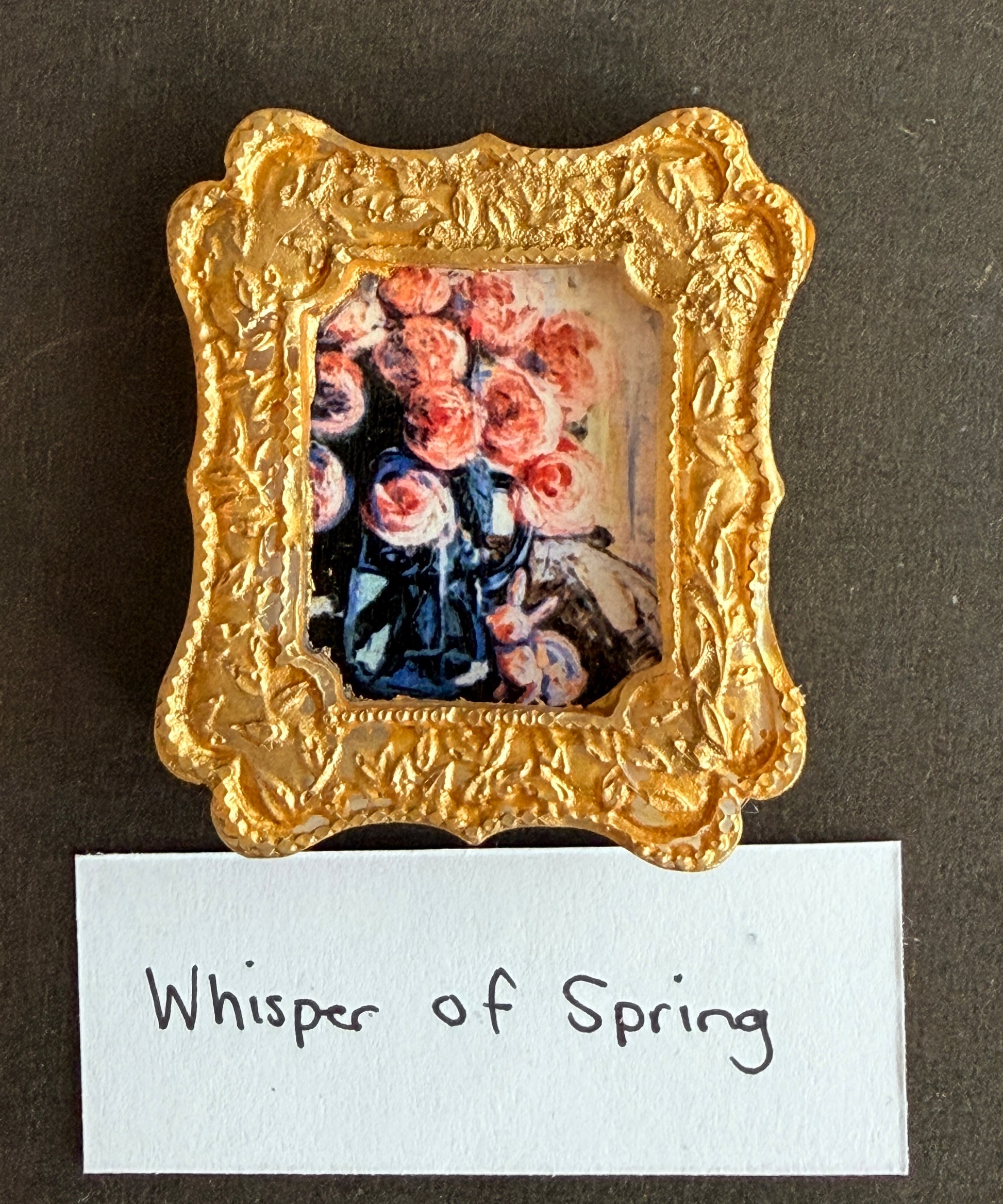 A painting of pink roses in a vase with a small glass bunny. The painting is in a gold frame magnet. The words Whisper of Spring are listed below it. 