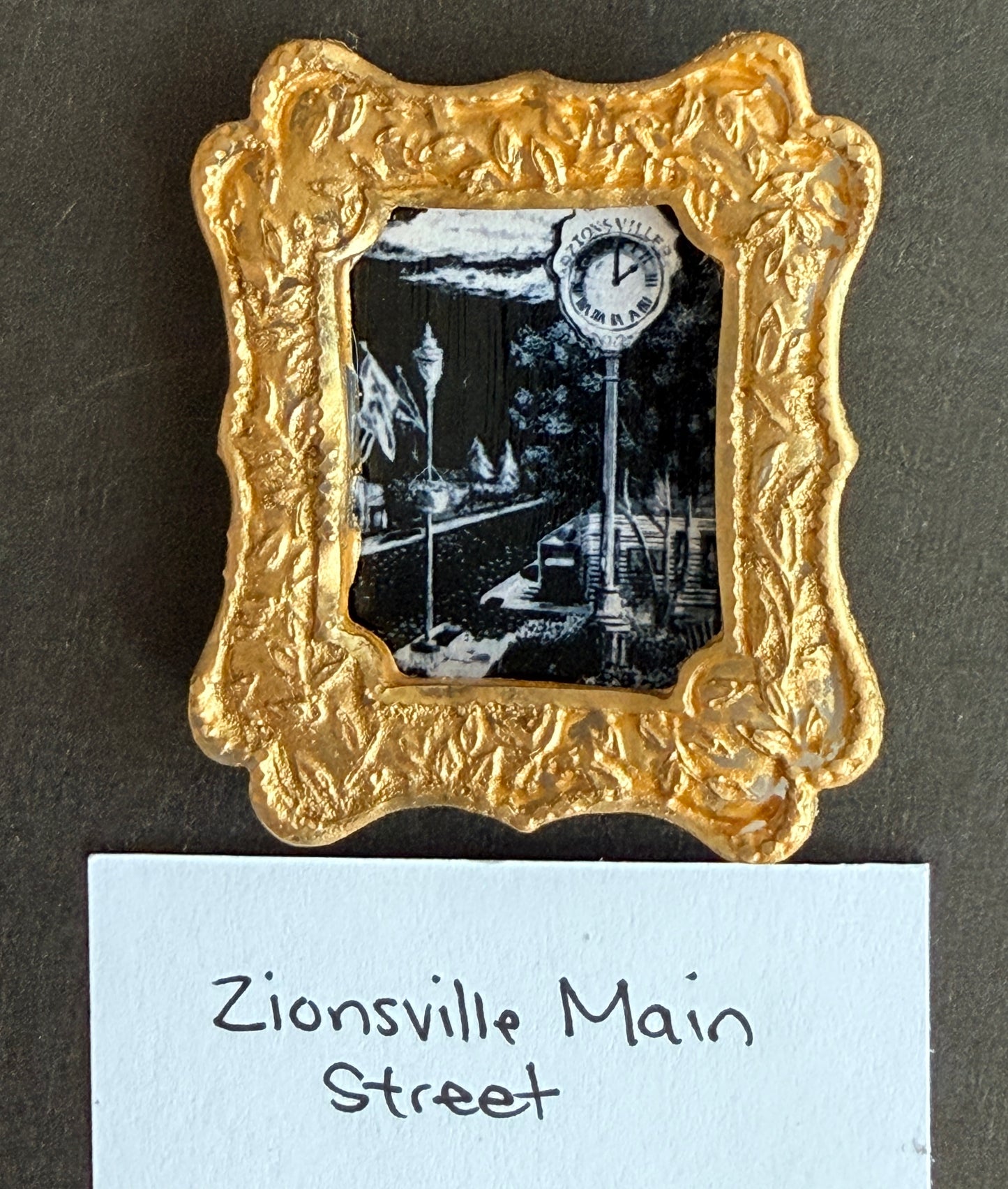 A black and white mainstreet art image in a gold frame with the words Zionsville Main street below it