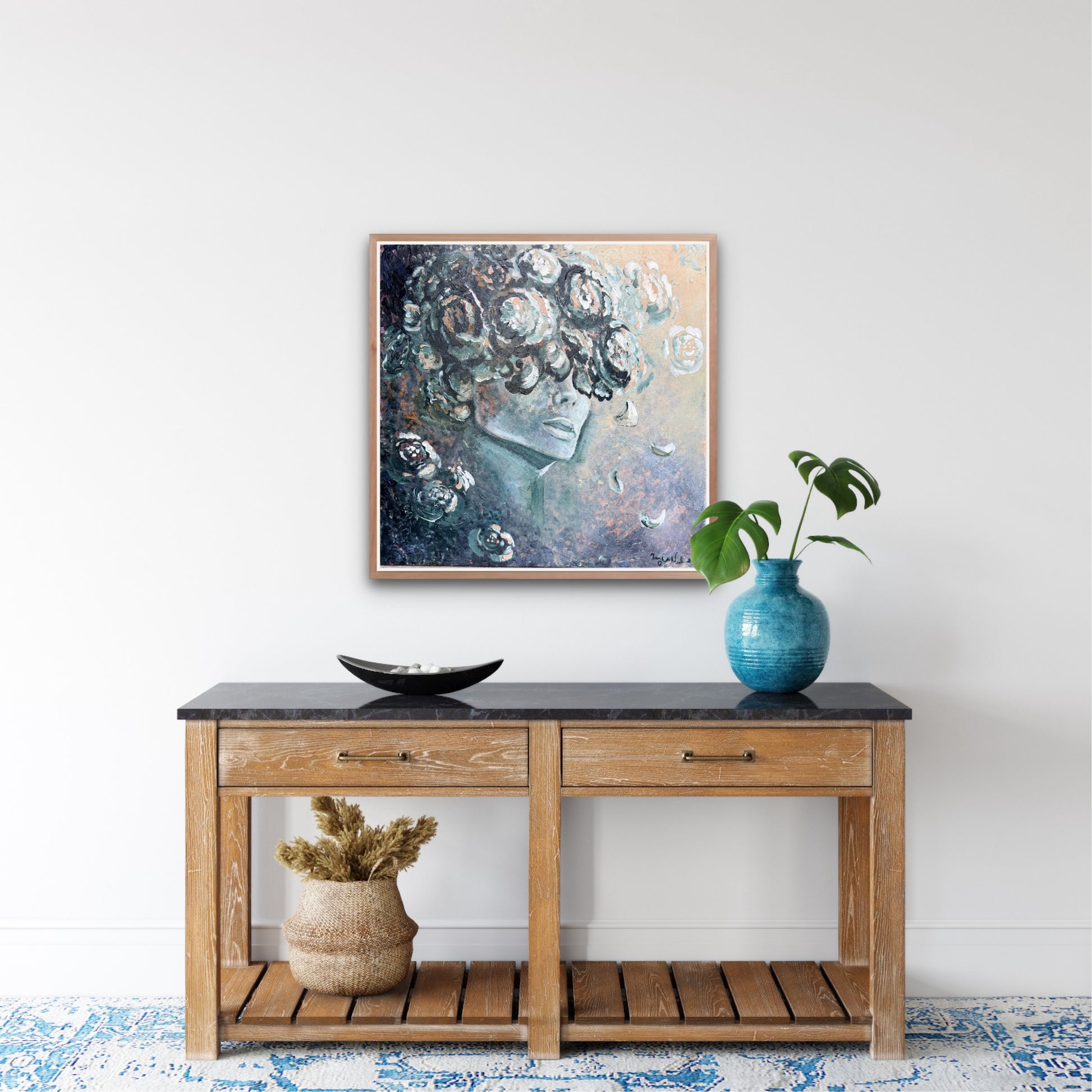 a modern female painting surrounded in florals in blues and neutral tones hangs on a white wall above a console table