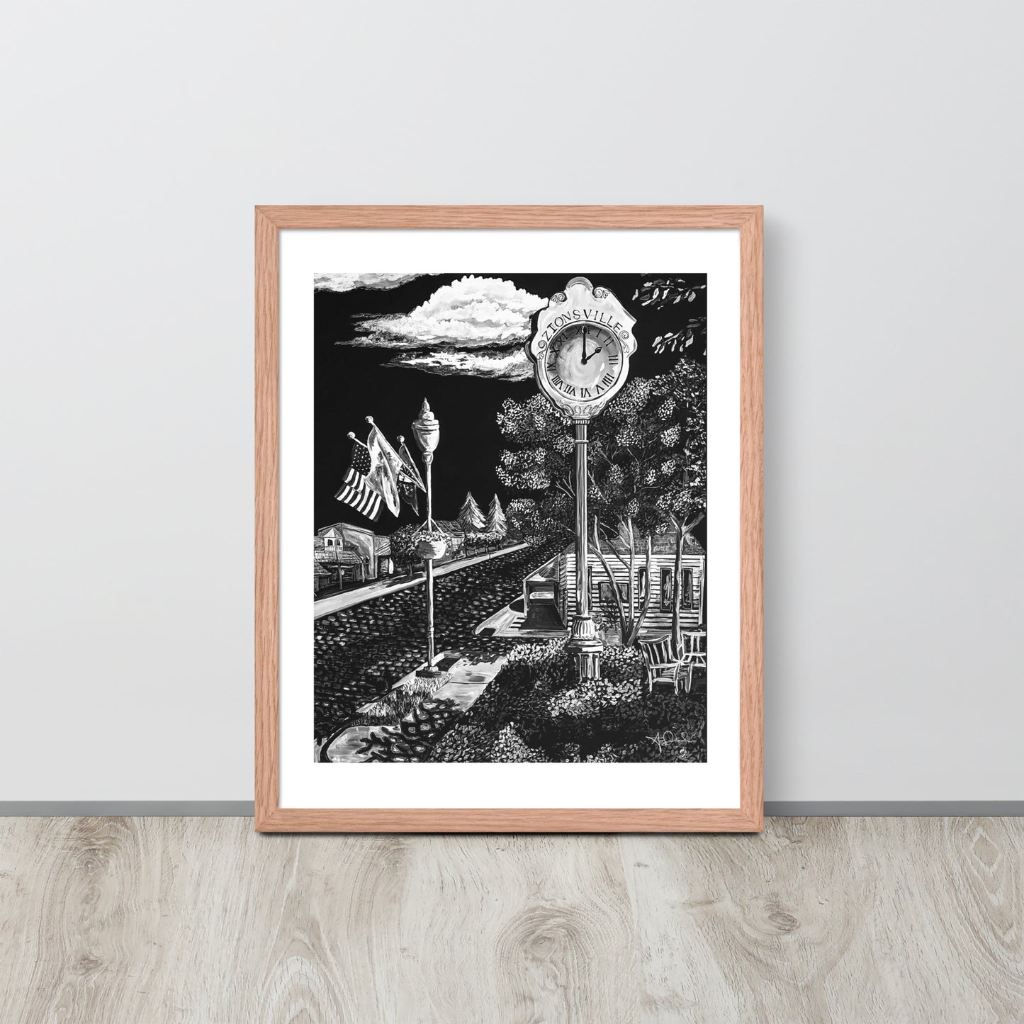 matte black and white framed art print of small town in red oak frame leaned up against gray wall on light toned wood floor