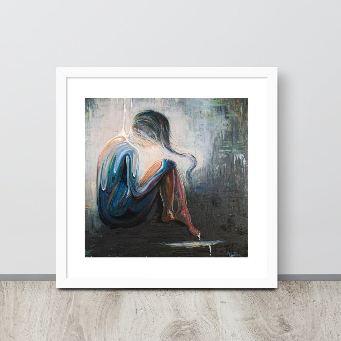 An art print of an abstract woman is framed in a white frame and sitting up against a gray wall on a neutral wood floor