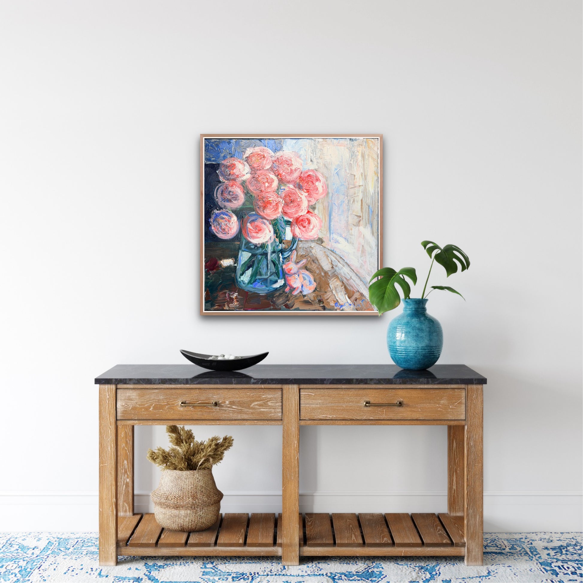framed floral painting hangs over a decorated console table in front of a white wall
